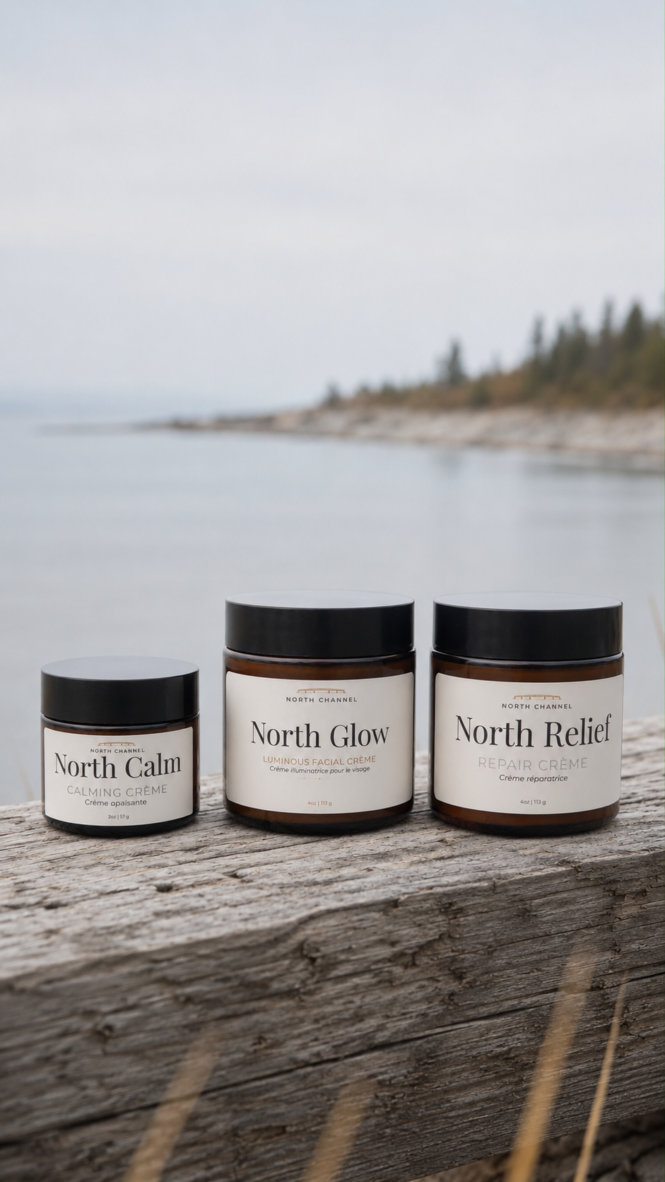 North Calm, North Glow, and North Relief crèmes standing on weathered driftwood, the sun low over open water behind them