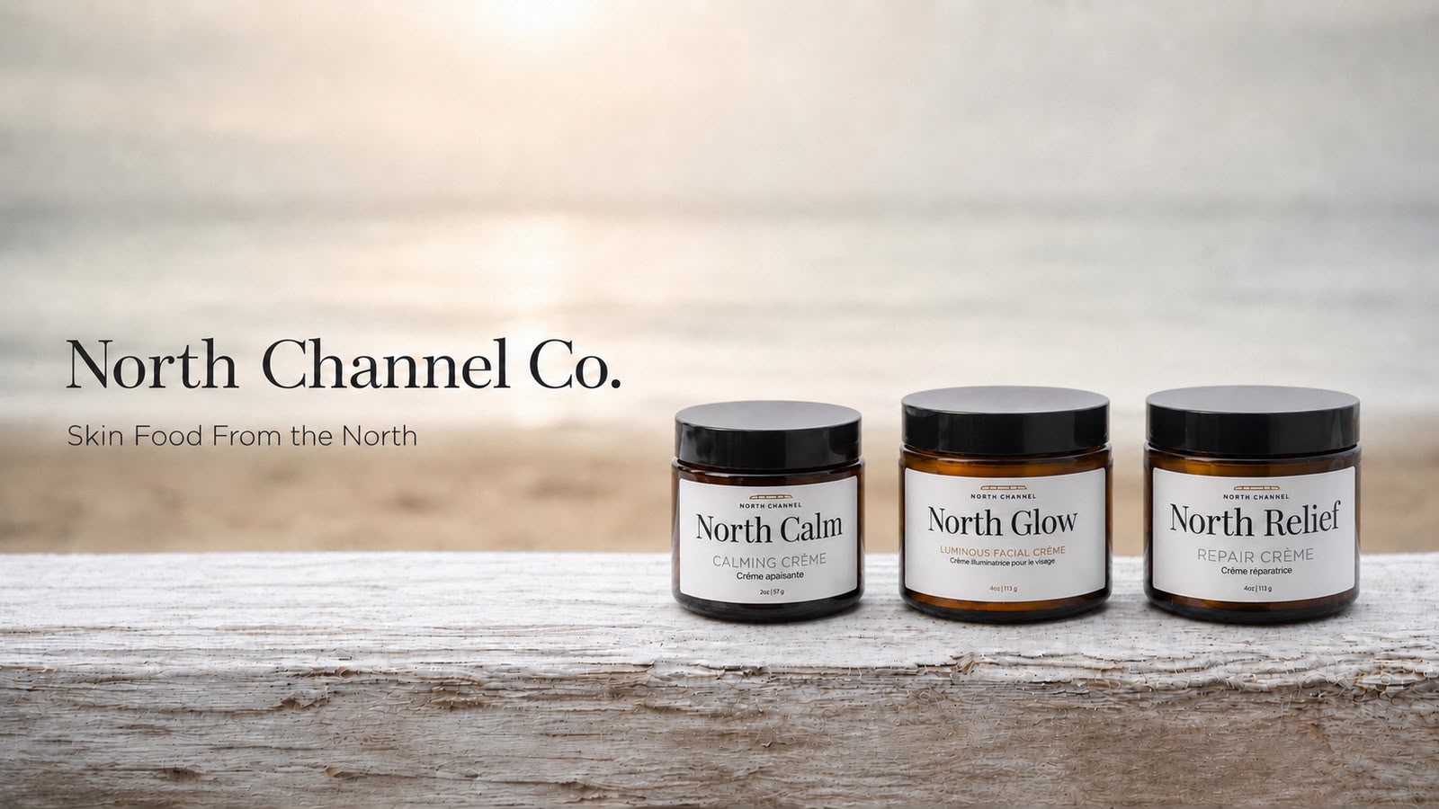North Calm, North Glow, and North Relief crèmes standing on weathered driftwood, the sun low over open water behind them